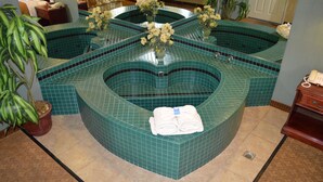 A spa area with a central hot tub surrounded by a tiled floor, a potted plant, and a telephone on a wooden table. - Dynasty Suites Redlands (Redlands)