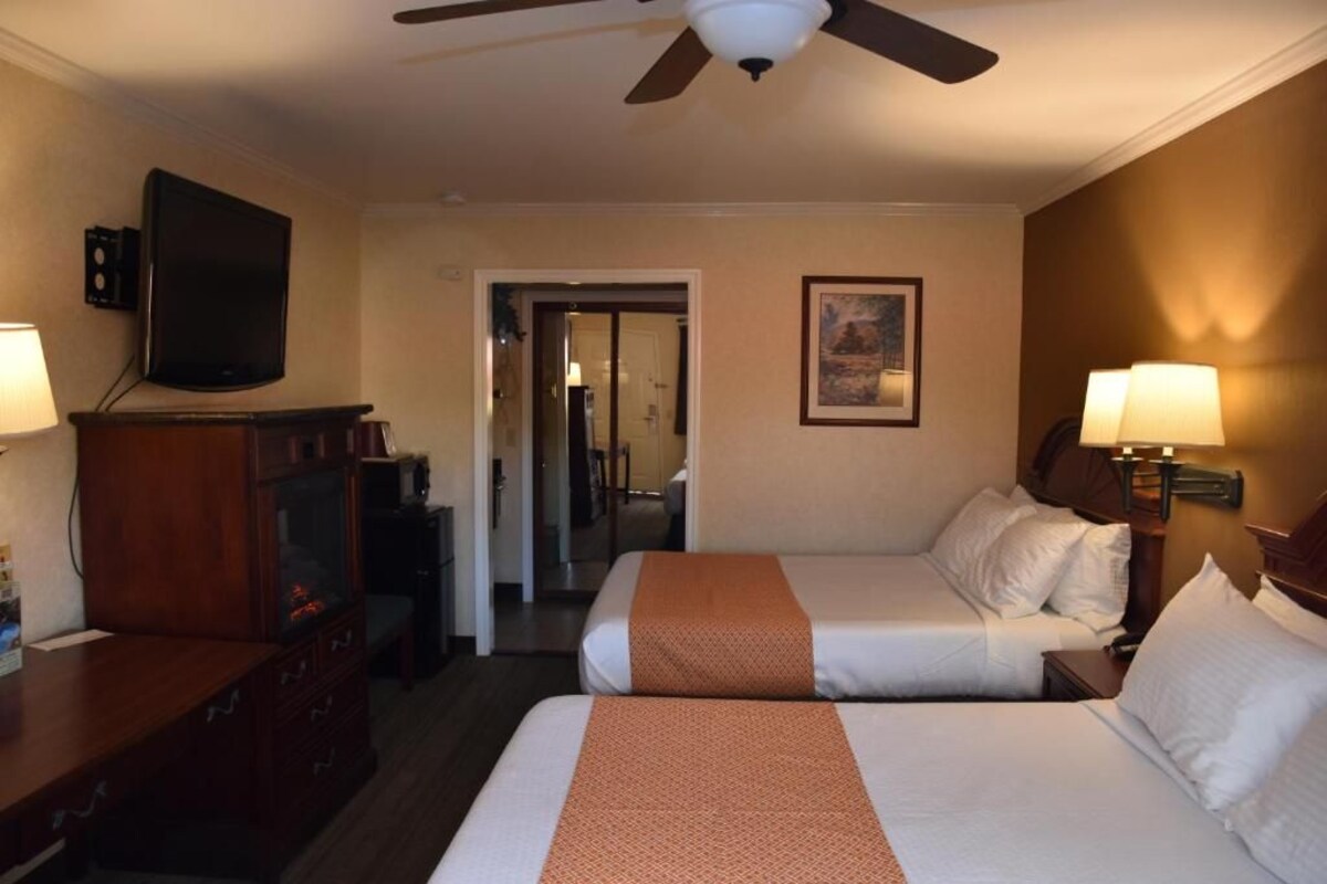 Habitación de hotel con dos camas, televisor, escritorio, ventilador de techo y puerta que da a otra habitación.