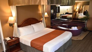 A hotel room with a large bed, a wooden nightstand with a phone, a bathroom with a bathtub, and a mirror reflecting the room. - Dynasty Suites Redlands (Redlands)