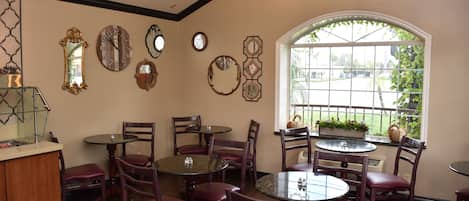 Un área de comedor con varias mesas y sillas, una barra y relojes decorativos en la pared.