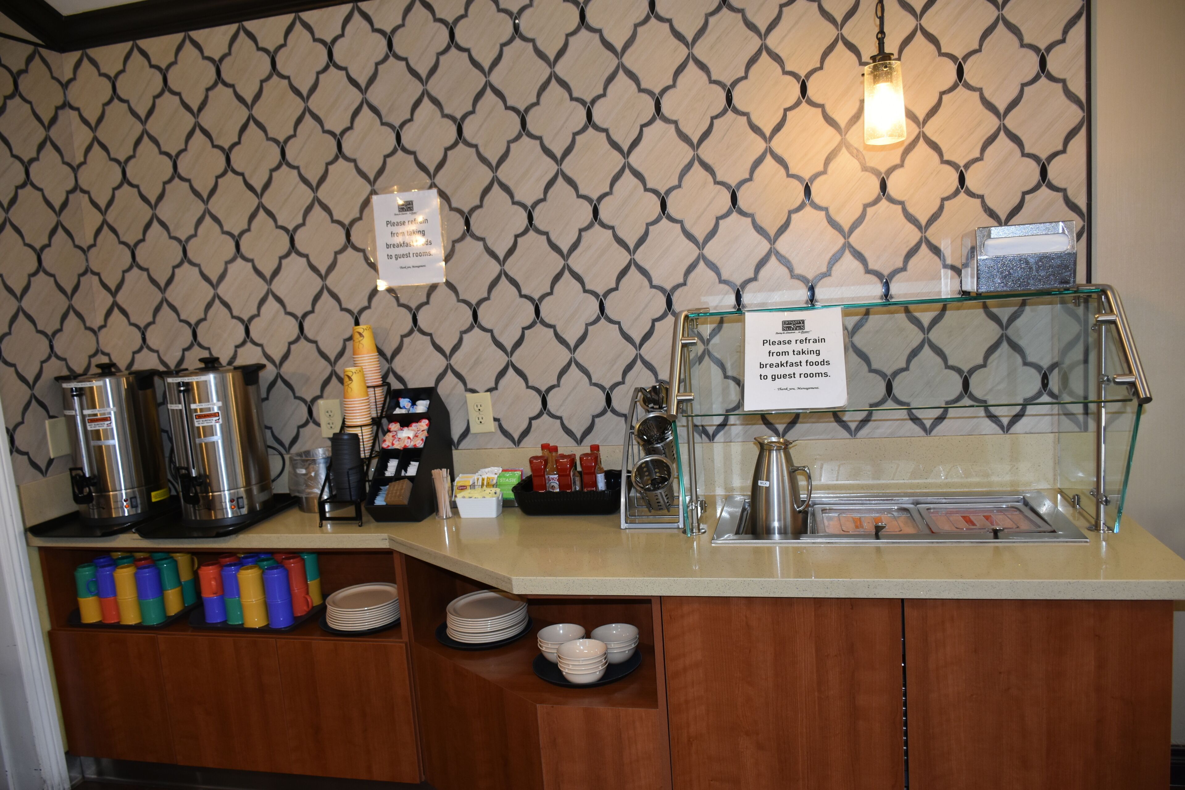 A breakfast bar with coffee machines, condiment dispensers, and a sign requesting no breakfast foods in guest rooms.