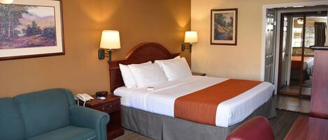 A hotel room with a bed, a desk, a chair, a sofa, and a painting on the wall.