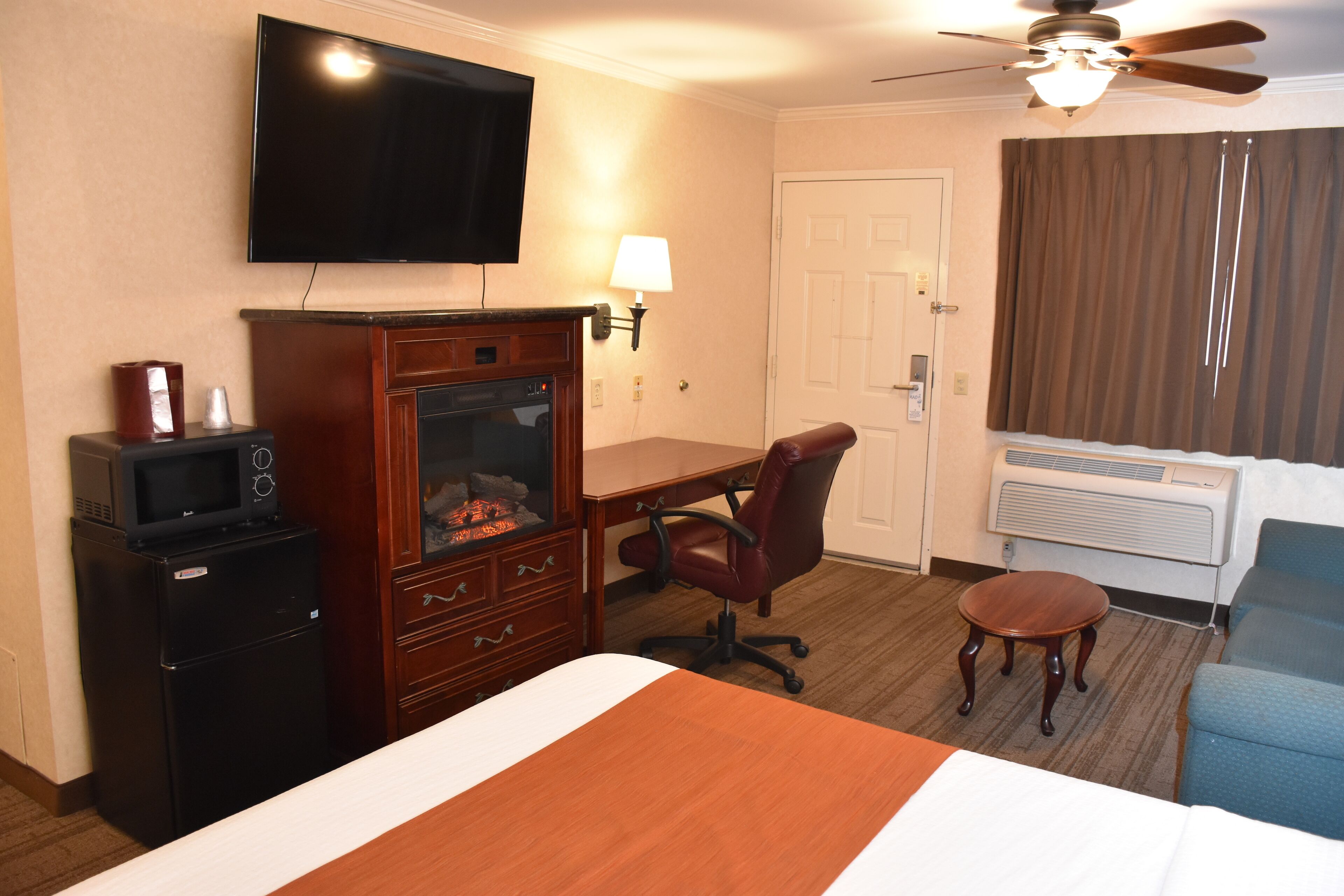 Habitación de hotel con cama, escritorio, silla, televisor, microondas, cómoda y aire acondicionado.