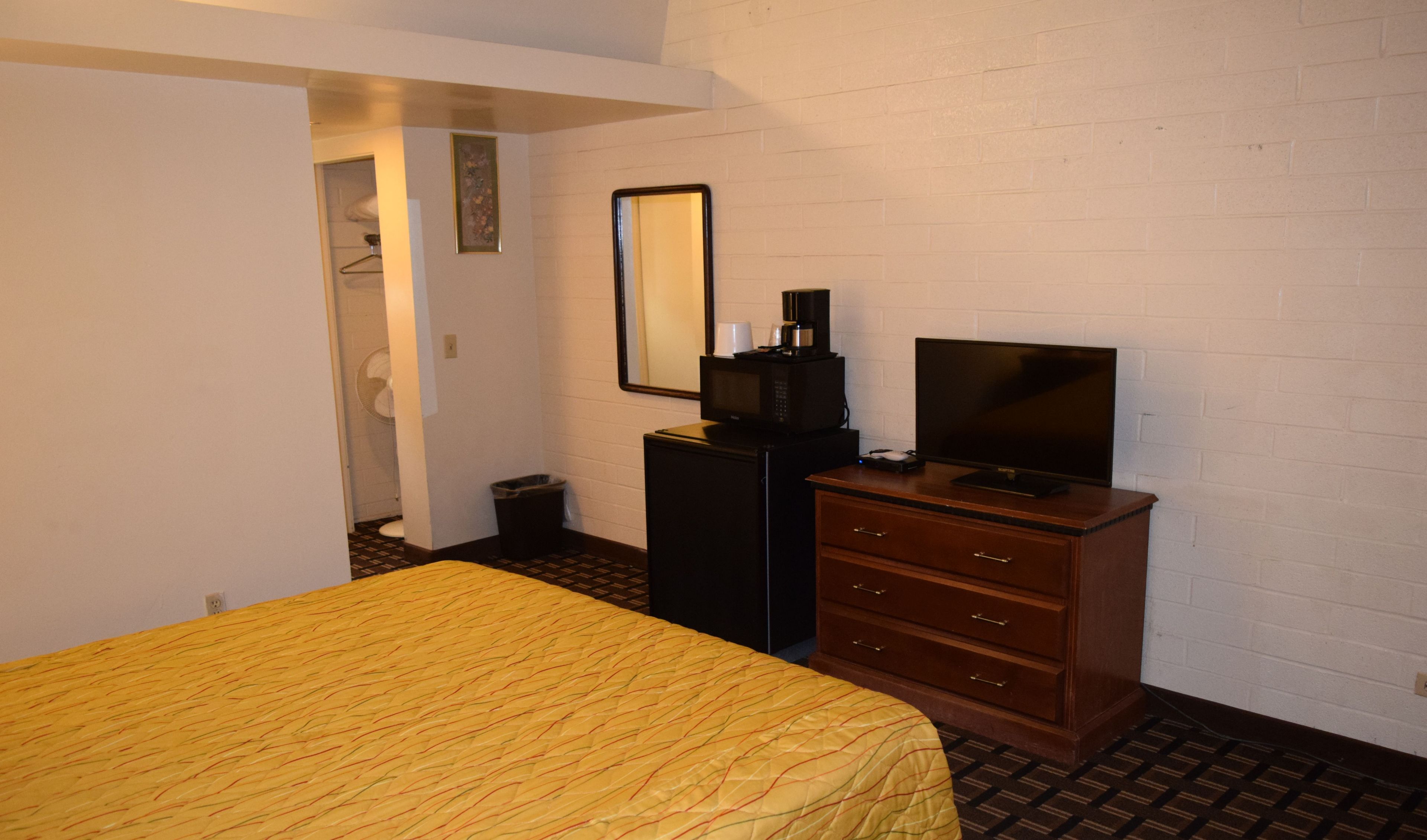 Quarto de hotel com cama, cômoda, televisão, micro-ondas e lixeira.