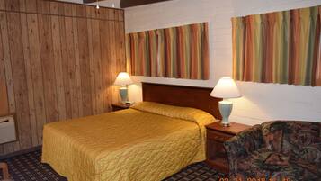 Habitación de hotel con pared de paneles de madera, cama con colcha amarilla, dos lámparas de noche, un sillón estampado y una cortina a rayas grande.