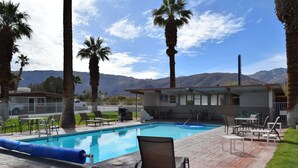 A swimming pool with lounge chairs and a building with a view of mountains.