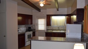 A kitchen with dark wooden cabinets, a white refrigerator, a granite countertop, and a ceiling fan.