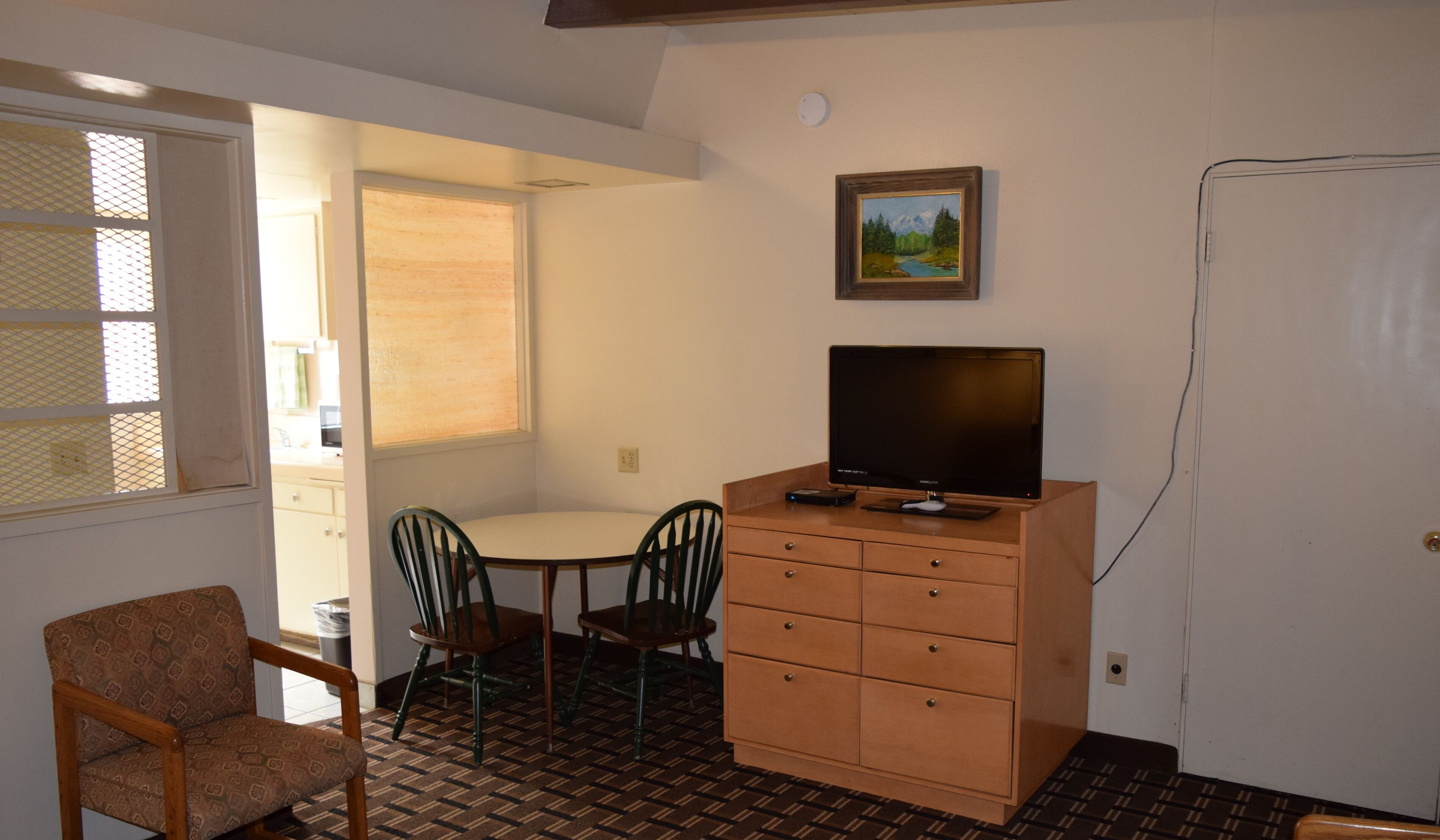 A small room with a single table, two chairs, a TV on a wooden cabinet, and a painting on the wall.