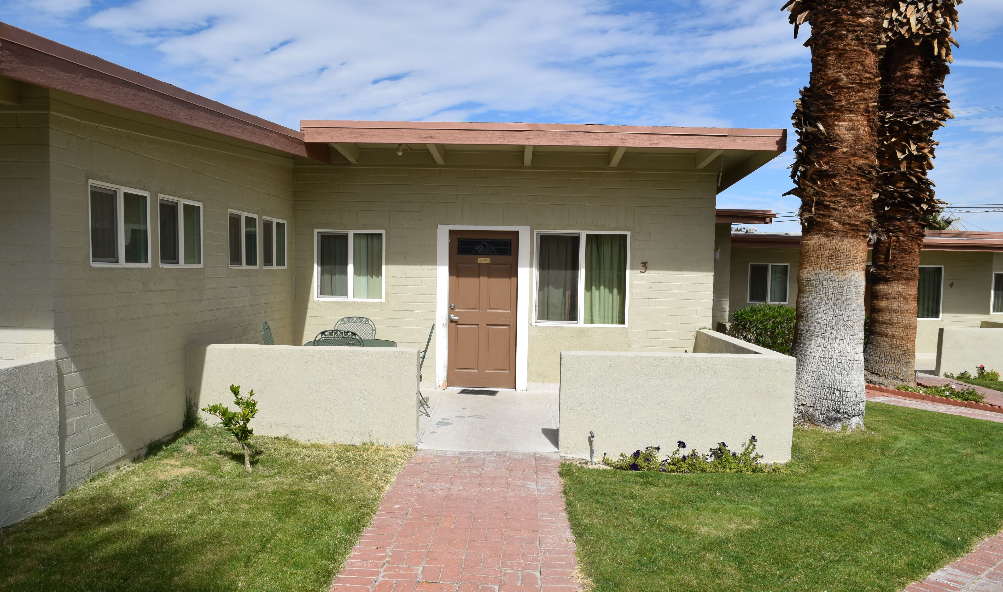 A two-story building with a brown door, windows, and a brick pathway leading to the entrance.