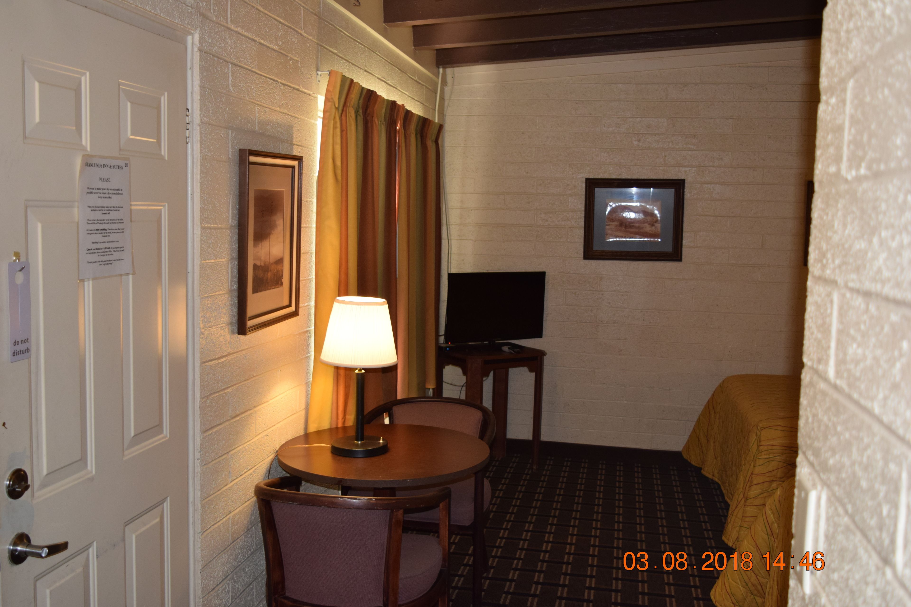 A hotel room with a bed, a television, a lamp, and a small table with chairs.