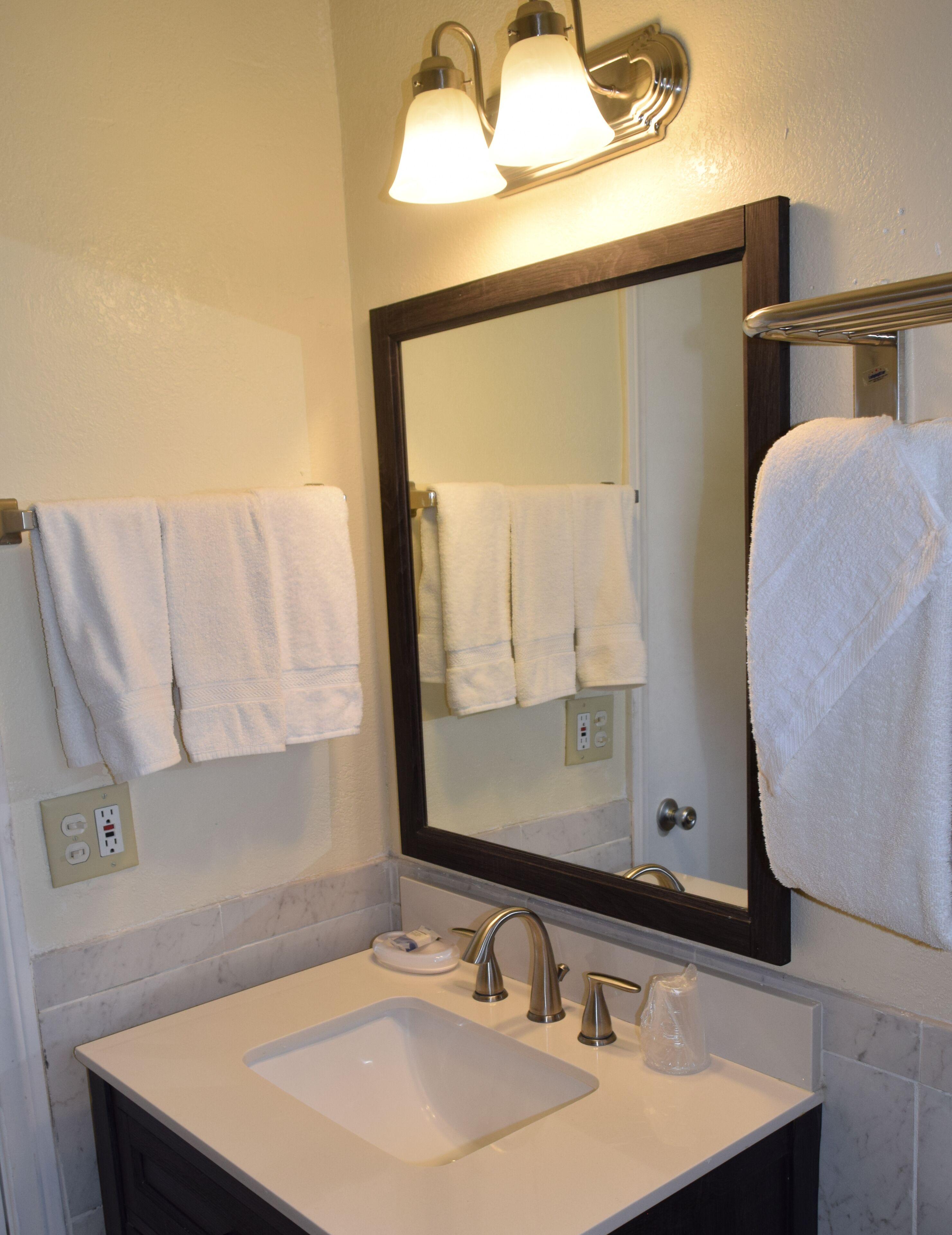A bathroom with a white sink, two faucets, a mirror, and two wall-mounted lights.