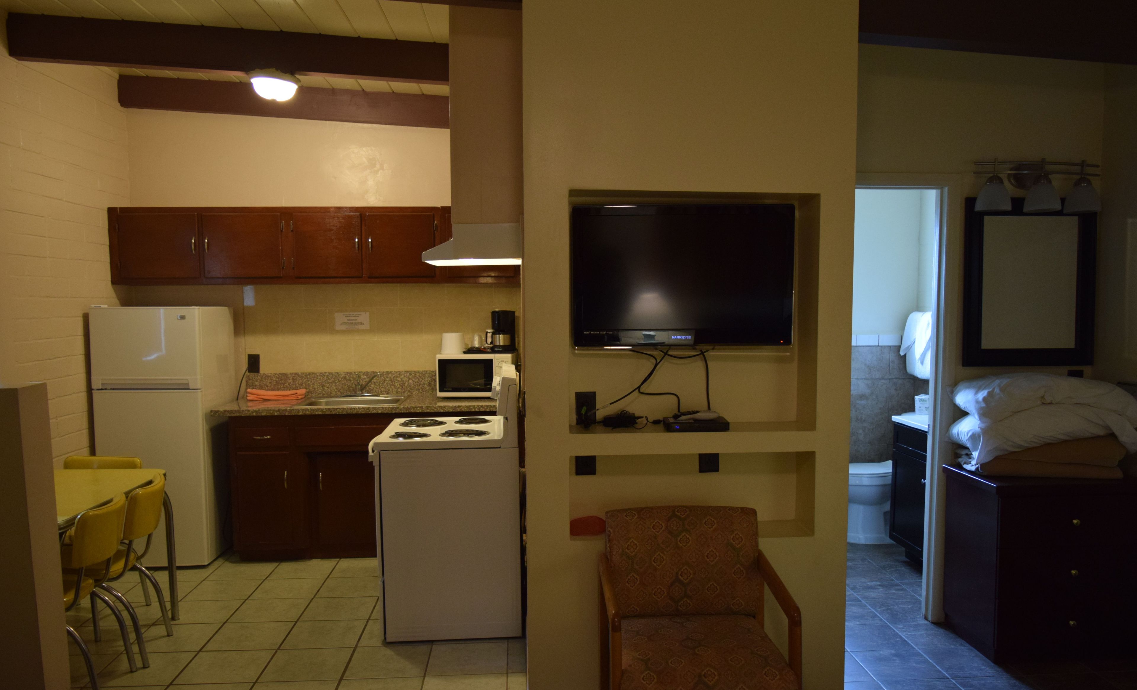 A compact kitchen with a refrigerator, stove, microwave, and a flat-screen TV mounted on the wall.