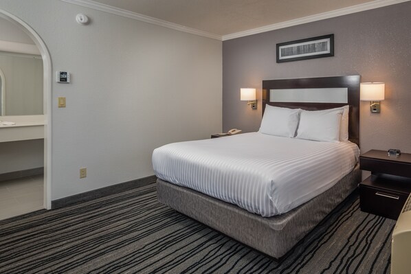 A hotel room with a large bed, two bedside tables, a nightstand, a wall-mounted phone, and a framed picture above the bed.