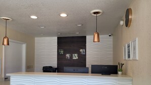 A reception desk with a modern design, featuring a textured wall, a flat-screen monitor, and a printer. - Redwood Creek Inn (Redwood City)