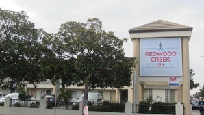 A sign for Redwood Creek Inn with a tree and a parking sign nearby. - Redwood Creek Inn (Redwood City)
