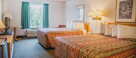 Une chambre d’hôtel avec deux lits, un bureau avec une lampe, une chaise, une fenêtre avec des rideaux et un tableau encadré au mur.