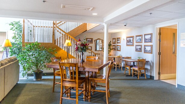 A spacious dining area with wooden tables and chairs, a staircase, and a potted plant.