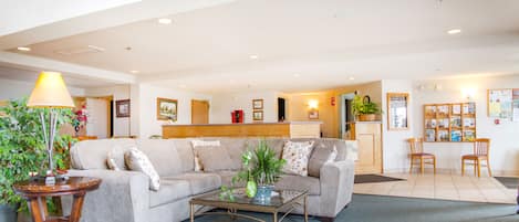 A spacious living area with a sofa, coffee table, and a lamp. There is a reception desk and a small dining area with chairs.