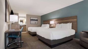 A hotel room with two beds, a desk, a chair, and a nightstand with a lamp.