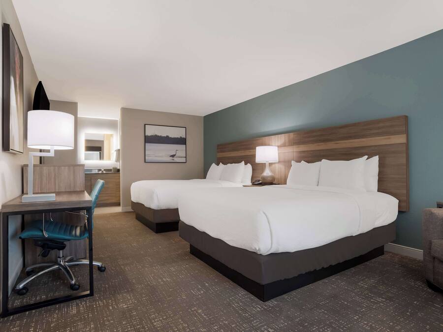 A hotel room with two beds, a desk, a chair, and a nightstand with a lamp.
