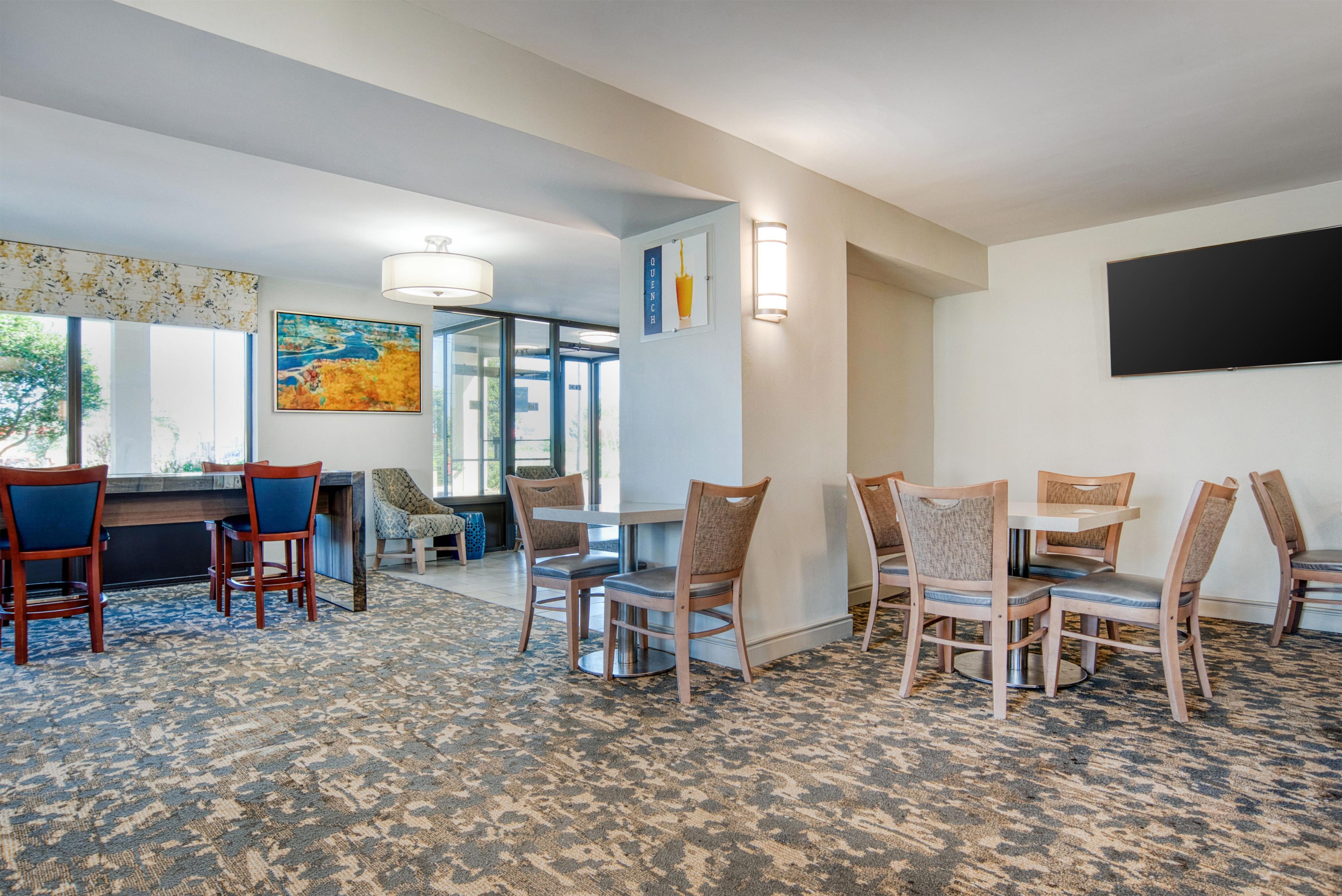 A hotel room with a dining area, a painting on the wall, and a view of the outdoors.