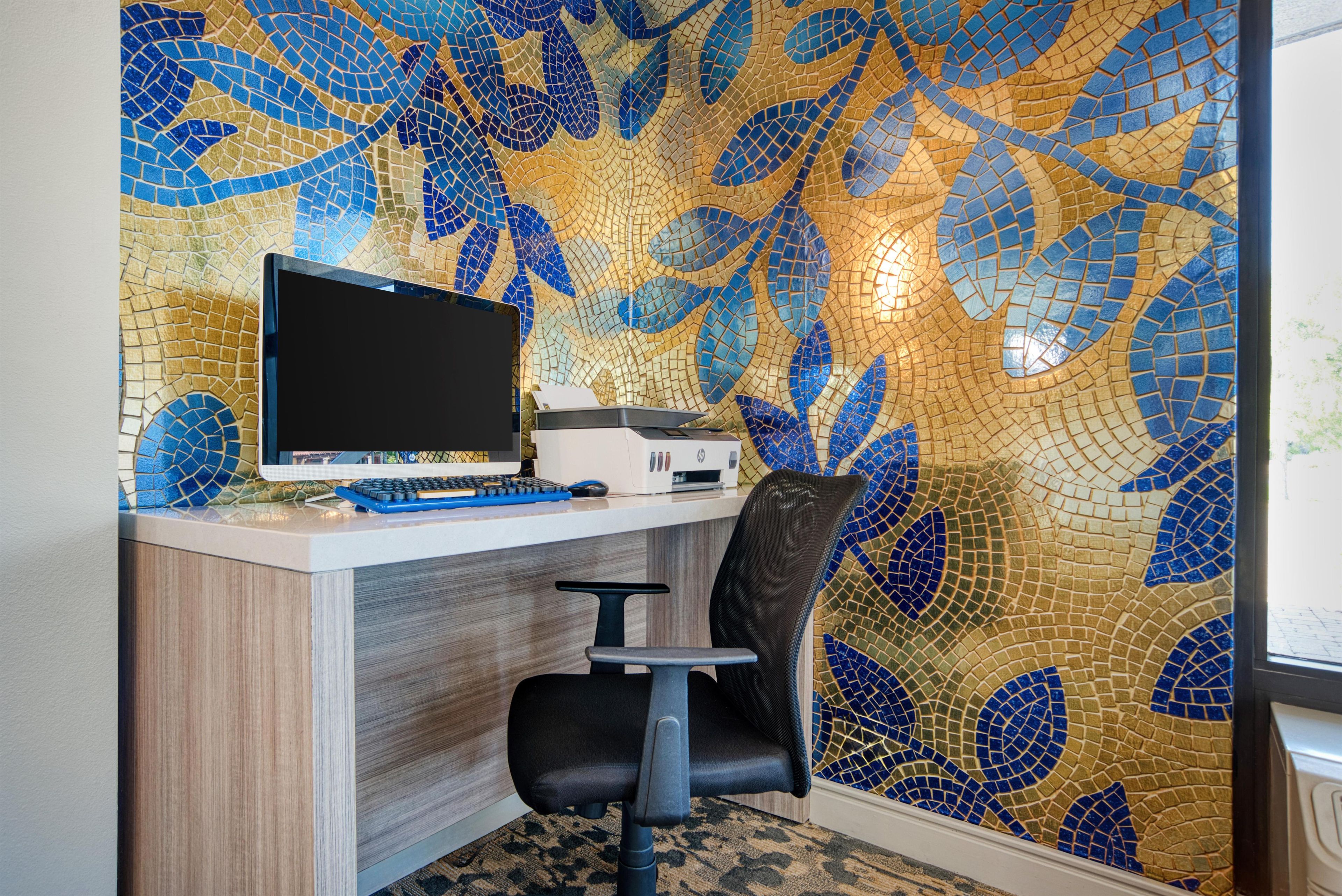 A workspace with a computer, printer, and office chair against a wall with a mosaic pattern.