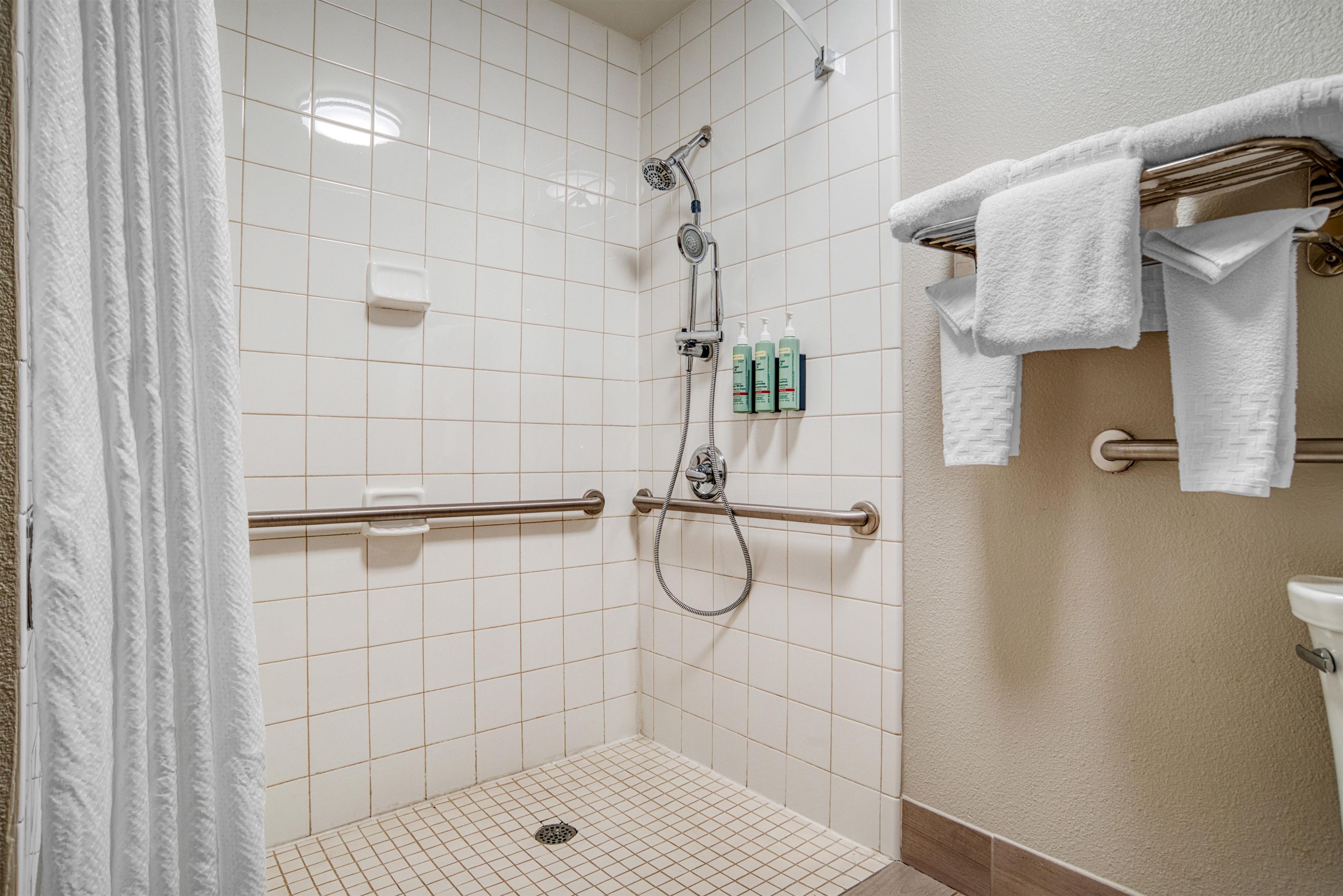 A shower area with white tiles, a grab bar, and a towel rack with towels.