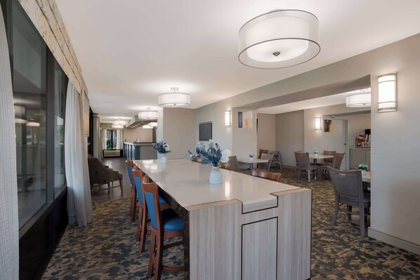 A modern hotel dining area with a long wooden table, blue upholstered chairs, and a vase of flowers.