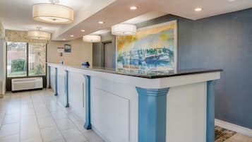A reception area with a long counter, multiple pendant lights, a large painting, and a view through a window.