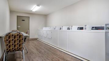 Une buanderie avec une rangée de machines à laver blanches, une chaise avec un coussin à motifs et une porte portant l’inscription « Réservé au personnel ».