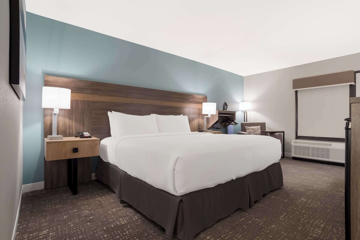 A hotel room with a large bed, two bedside tables with lamps, a flat-screen TV, and a built-in air conditioning unit.