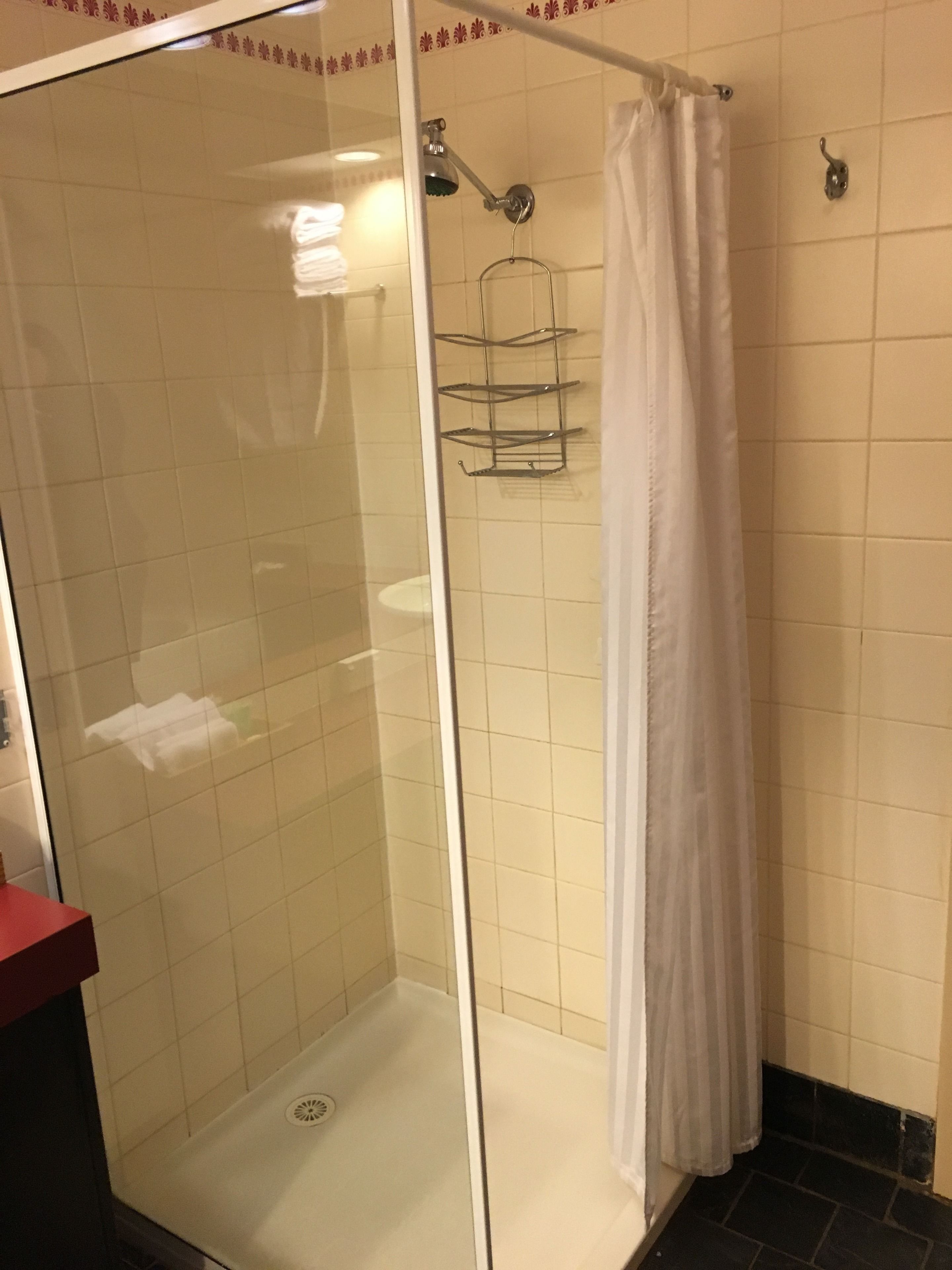 A glass-enclosed shower with a white curtain, tiled walls, and a metal rack.