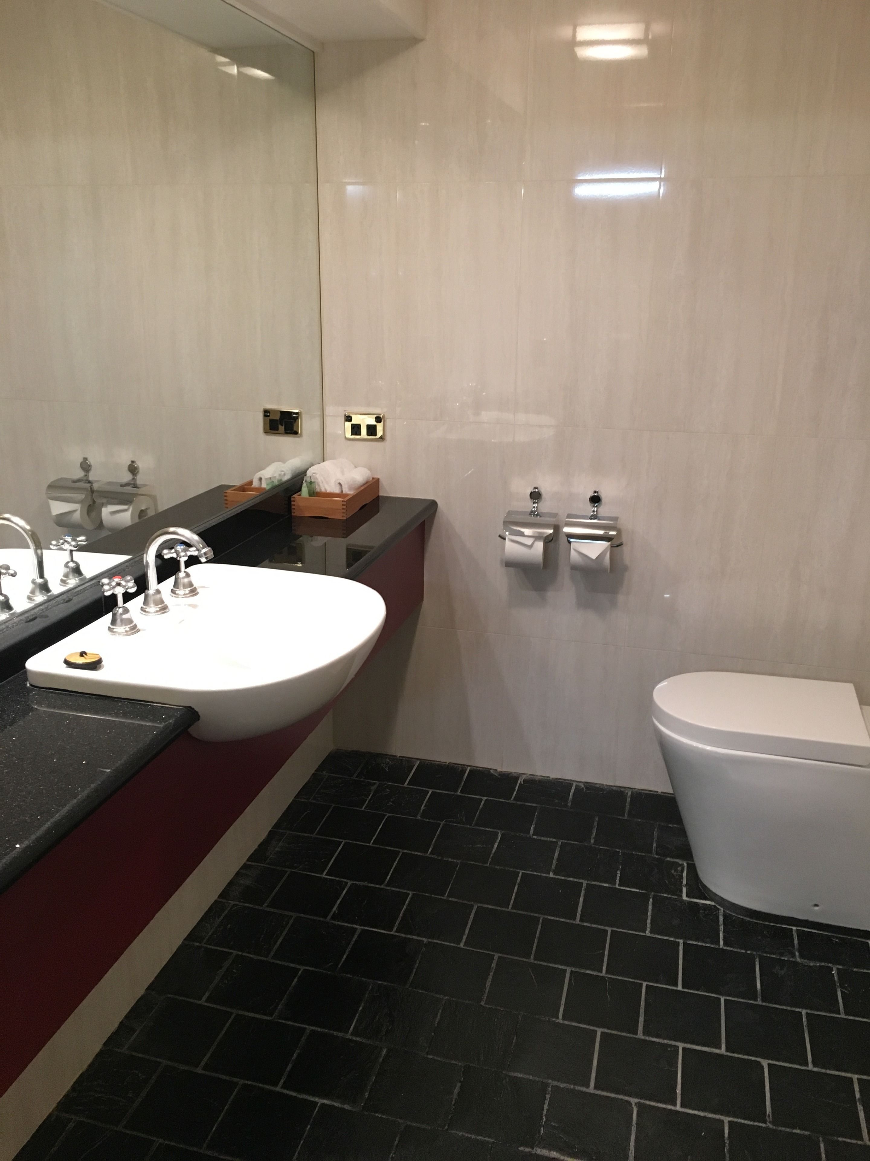 Een badkamer met een wit wastafelmeubel, een spiegel, een toilet en een vloer betegeld met zwart mozaïek.