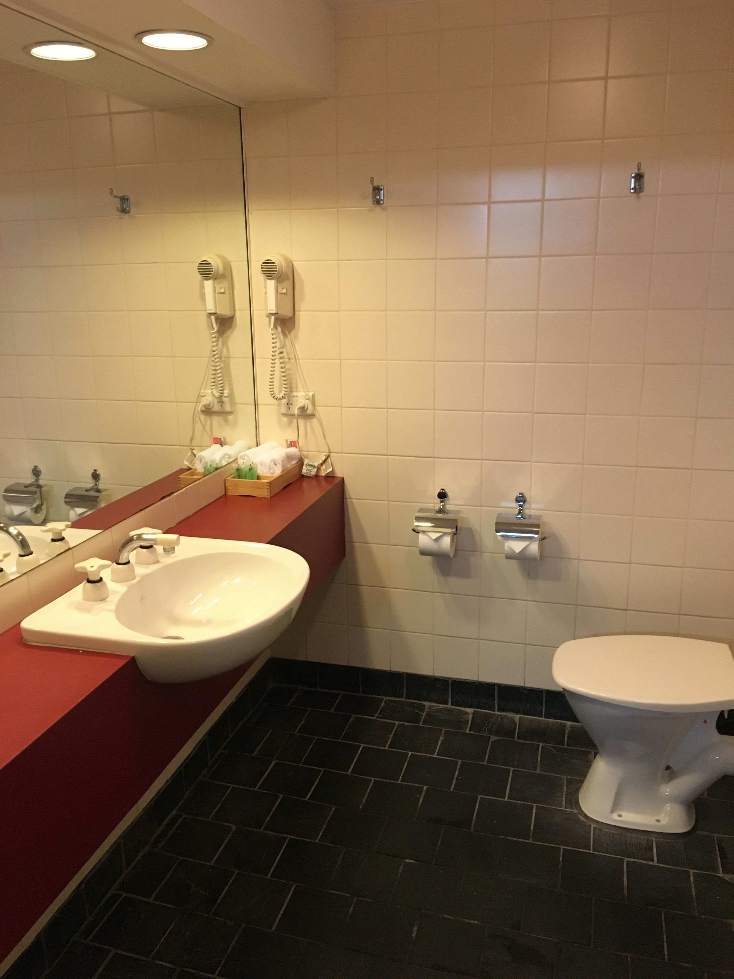 A bathroom with a white sink, a mirror, a toilet, and a hairdryer on the wall.