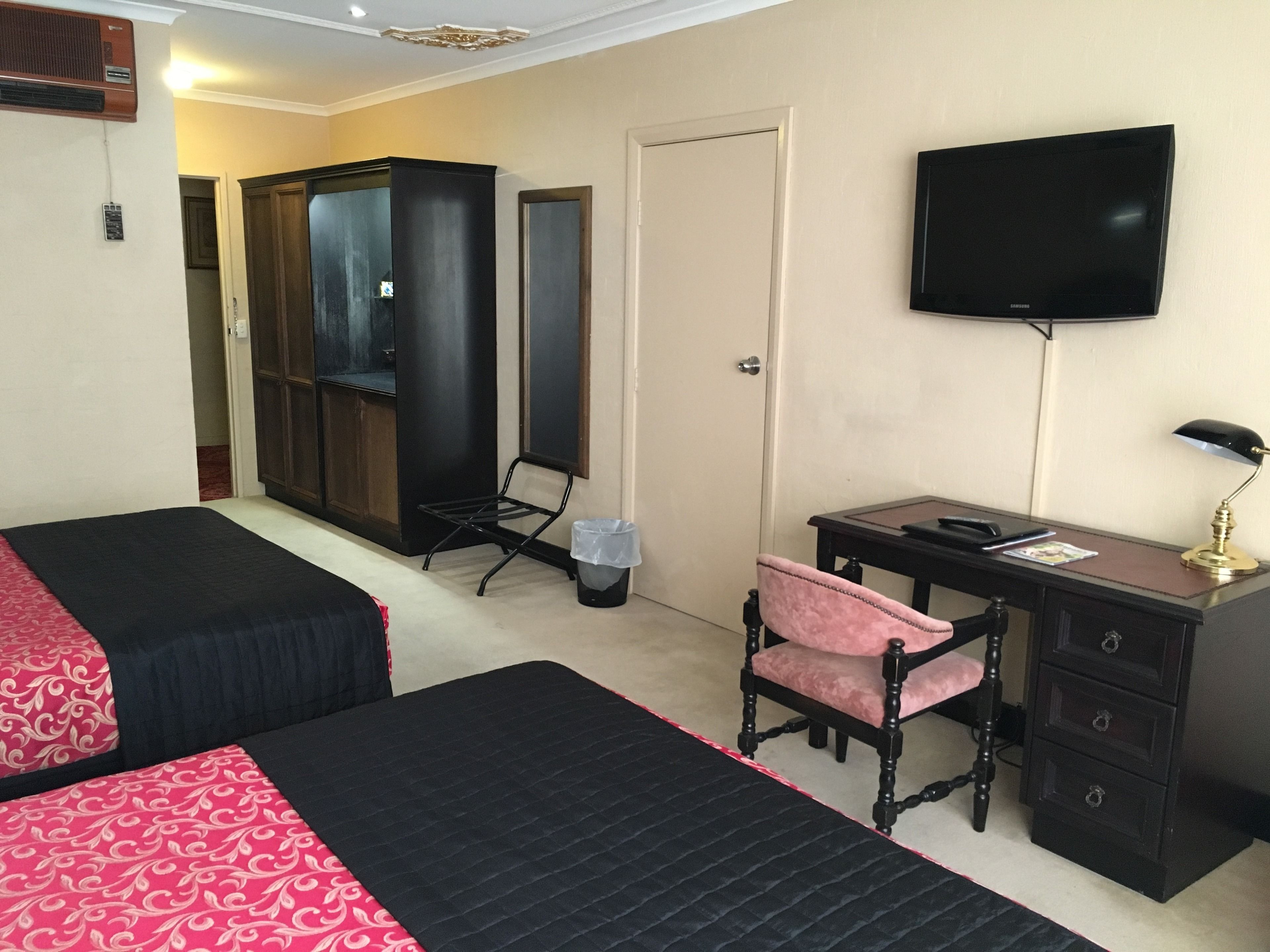 A hotel room with two beds, a desk with a chair, a TV, and a wardrobe.