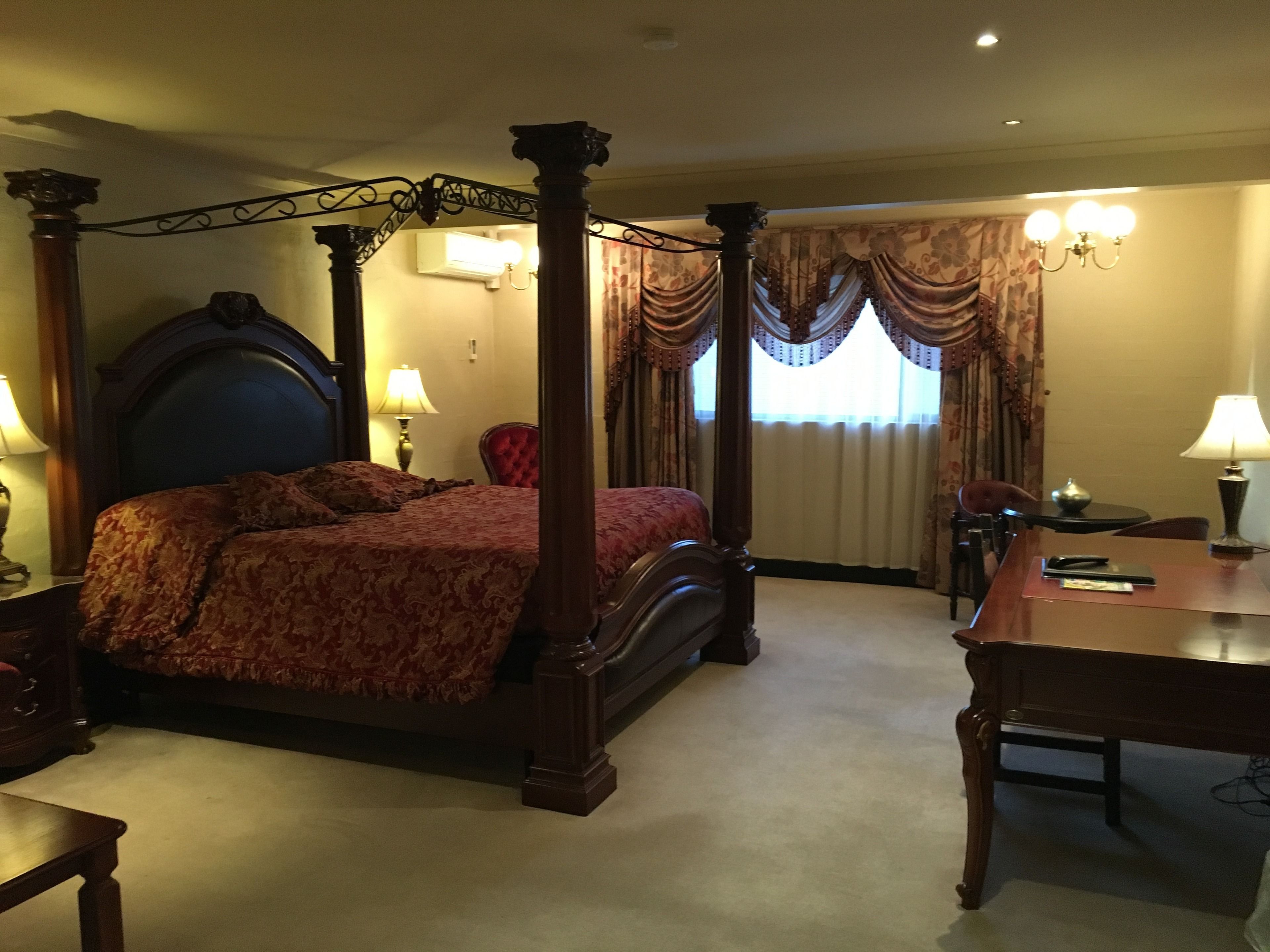 A four-poster bed with a headboard, a table, and a chair in a hotel room.