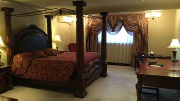 A four-poster bed with a headboard, a table, and a chair in a hotel room.