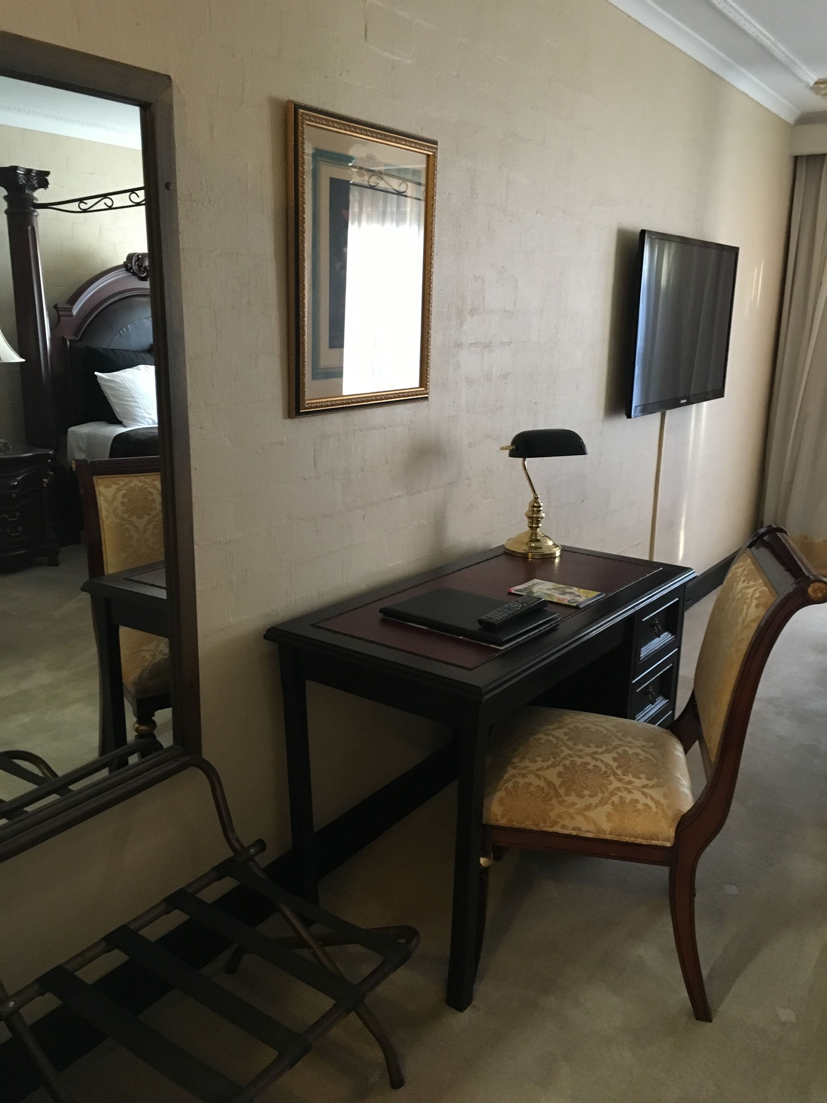 Ein Hotelzimmer mit Schreibtisch, Stuhl, Spiegel und Fernseher.