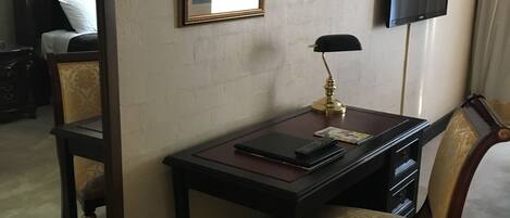 A hotel room with a desk, chair, mirror, and a television.