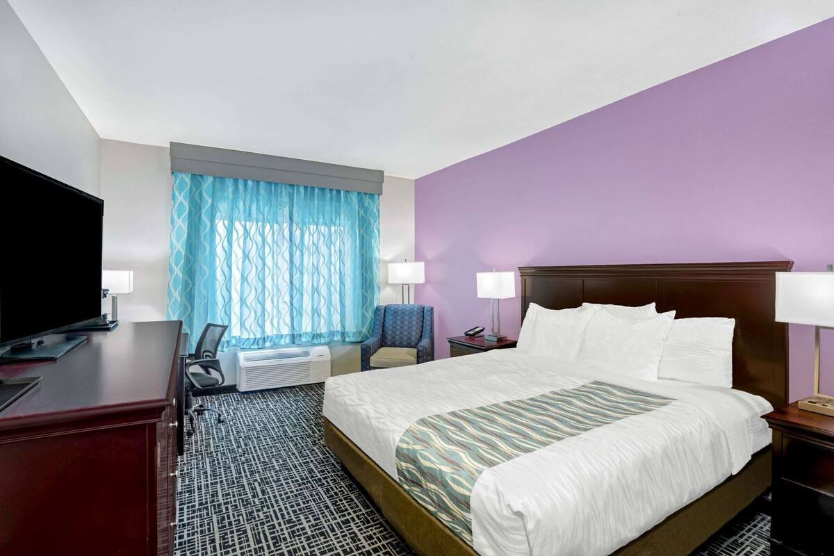 A hotel room with a bed, desk, TV, chair, and a window with curtains.
