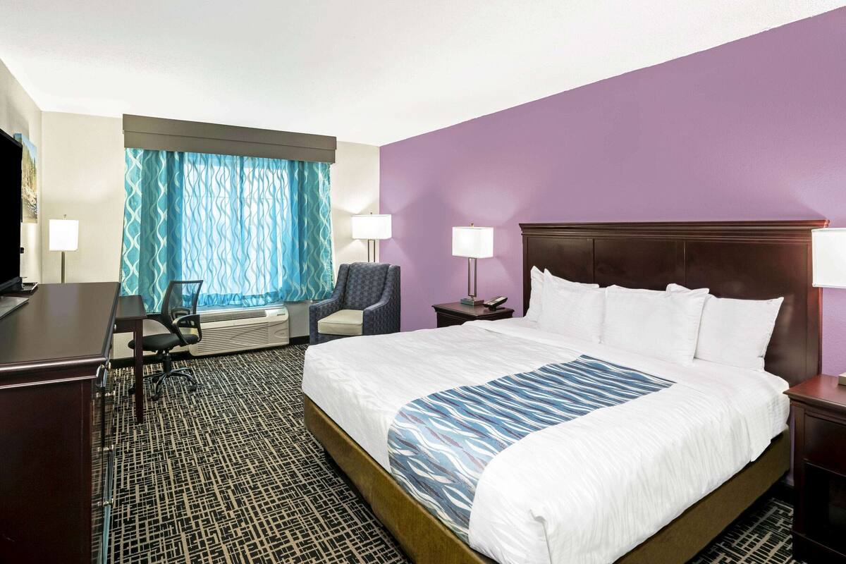 A hotel room with a large bed, a desk, a chair, a TV, and a window with curtains.