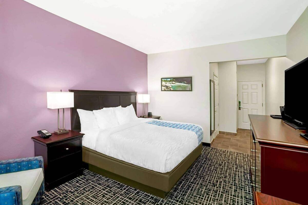 A hotel room with a bed, two bedside tables, a desk, a television, and a door.