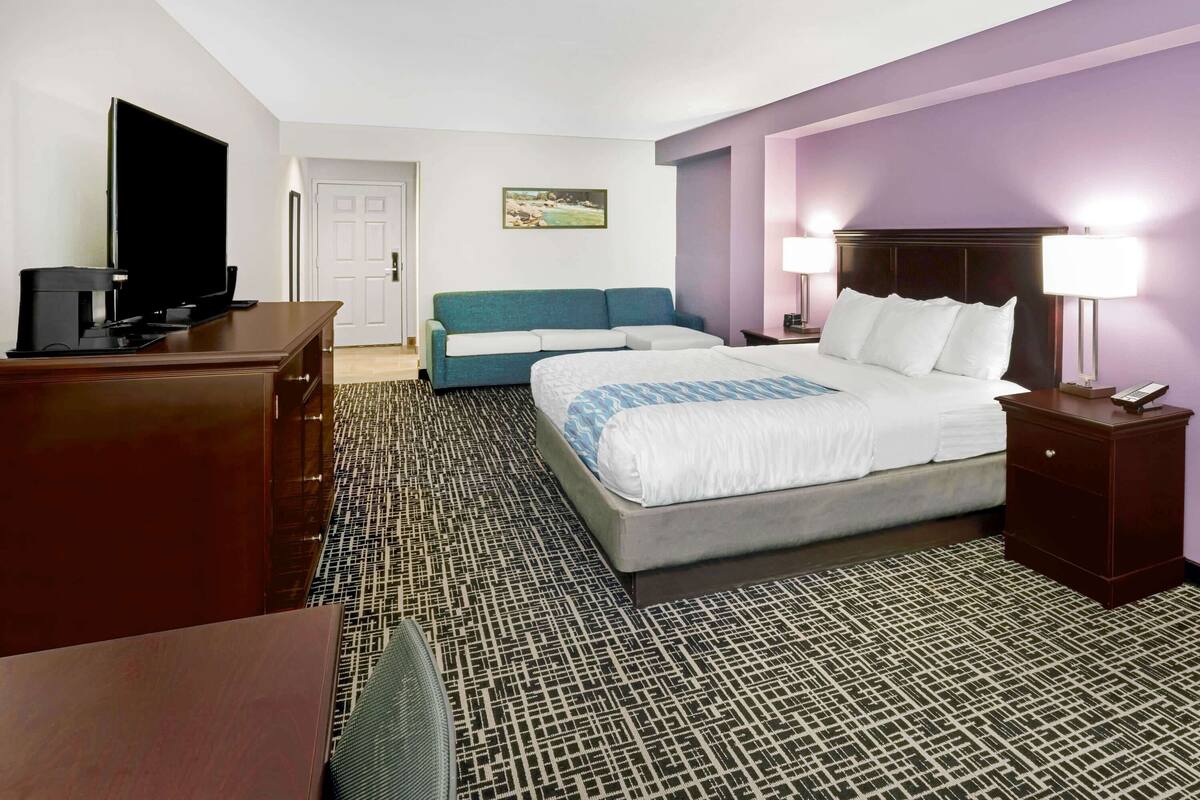 A hotel room with a large bed, a TV, a desk, and a couch.