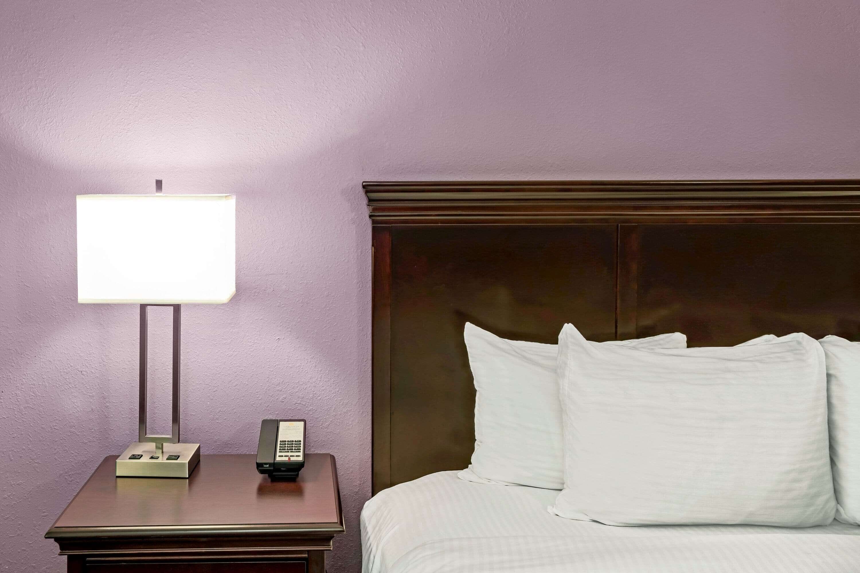 A hotel room with a bed, a nightstand, a lamp, and a telephone.