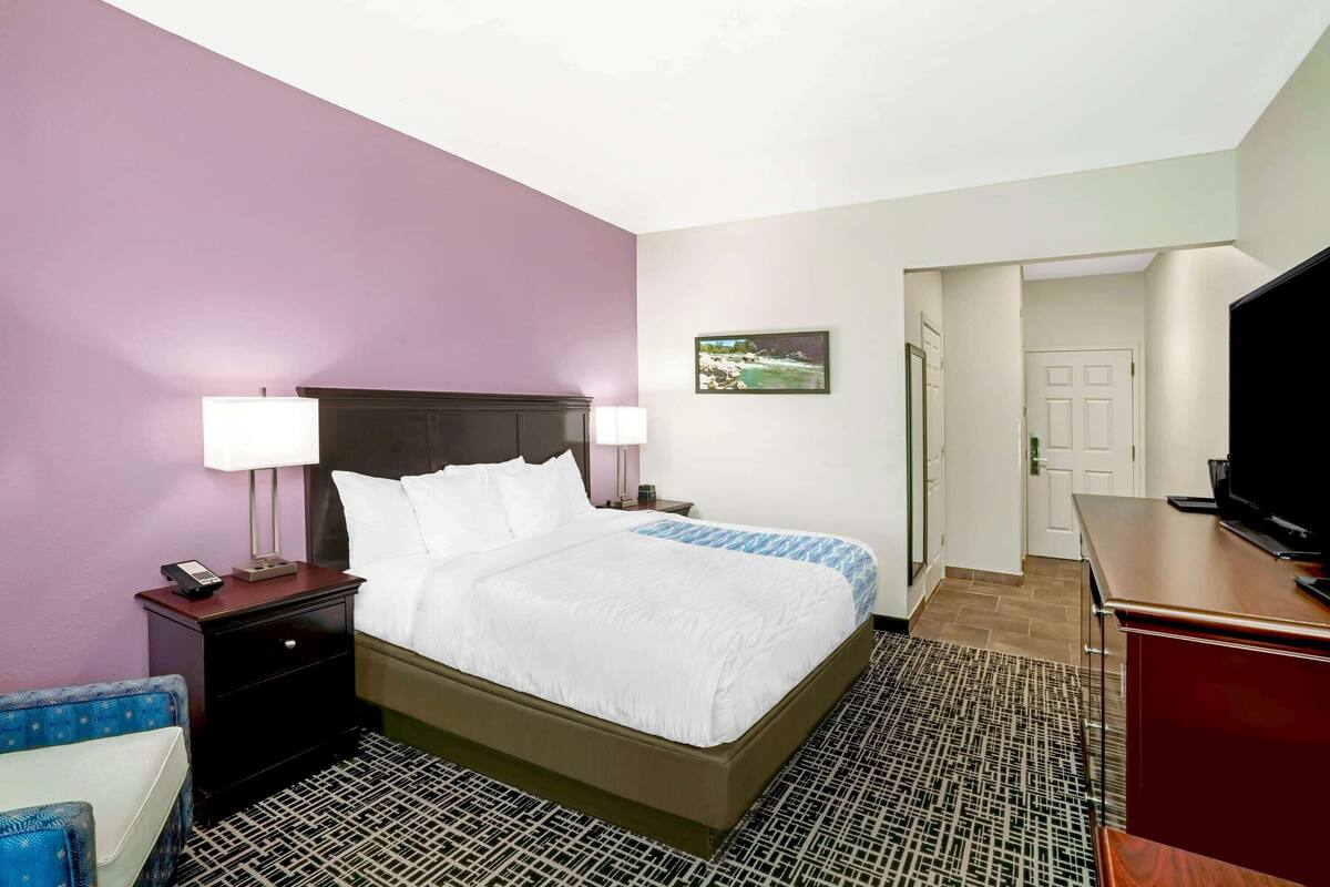 A hotel room with a bed, nightstand, lamp, and a television.
