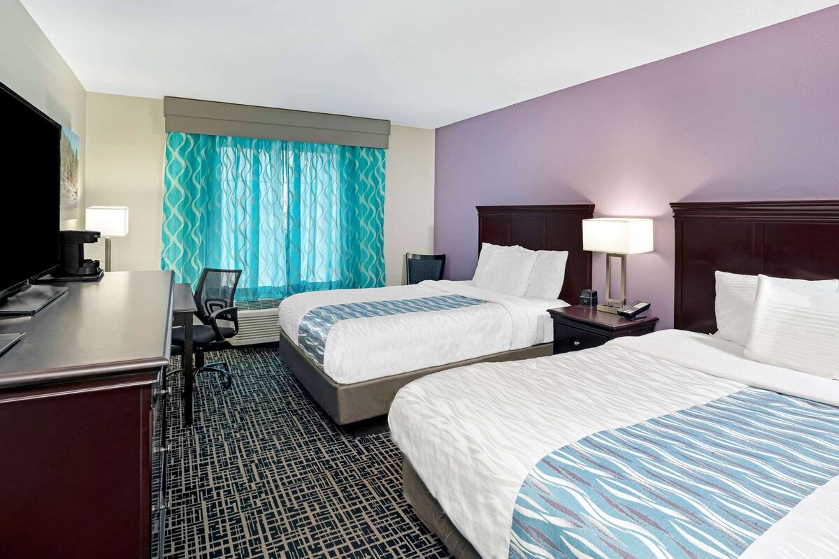 A hotel room with two beds, a desk, a chair, a TV, and a window with curtains.