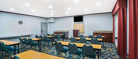 A conference room with multiple tables and chairs, a projector screen, and a carpeted floor.