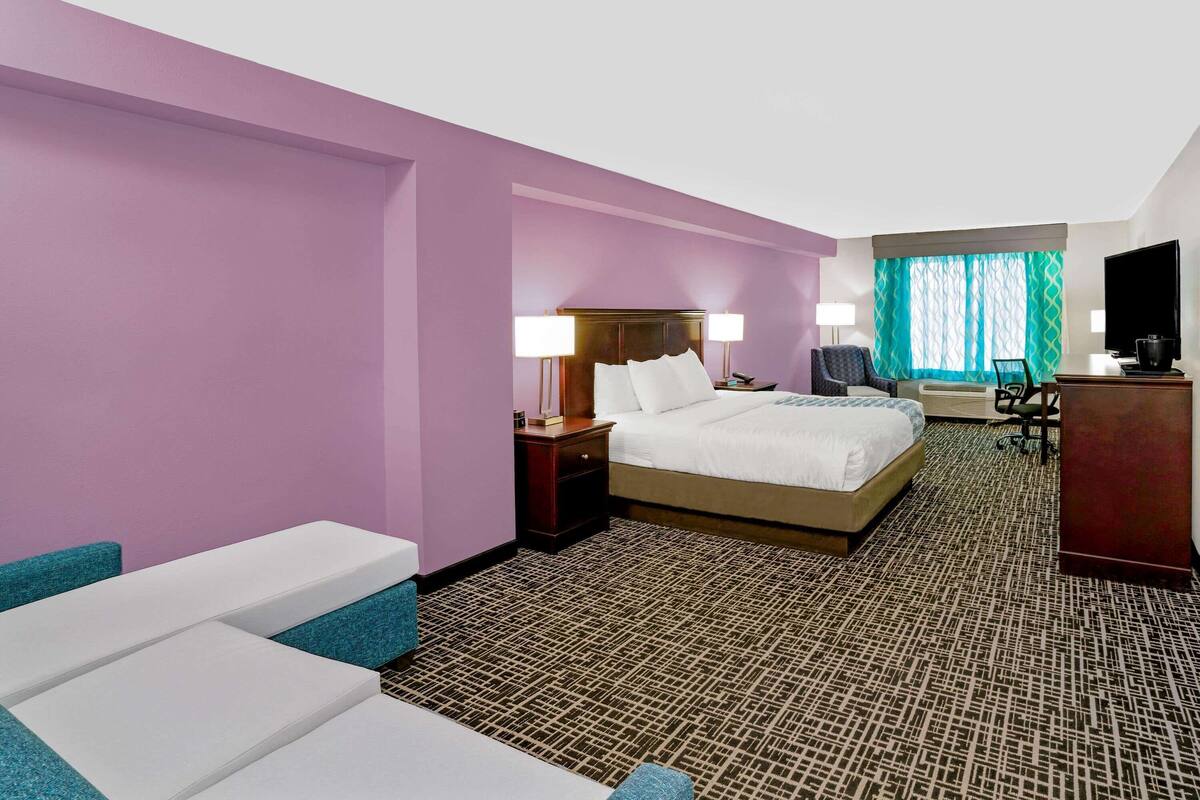A hotel room with a large bed, two bedside tables with lamps, a desk, a chair, and a television.