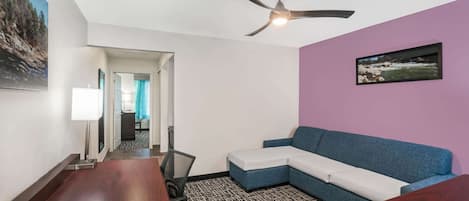 A hotel room with a ceiling fan, a sofa, a desk with a keyboard, and a patterned carpet.