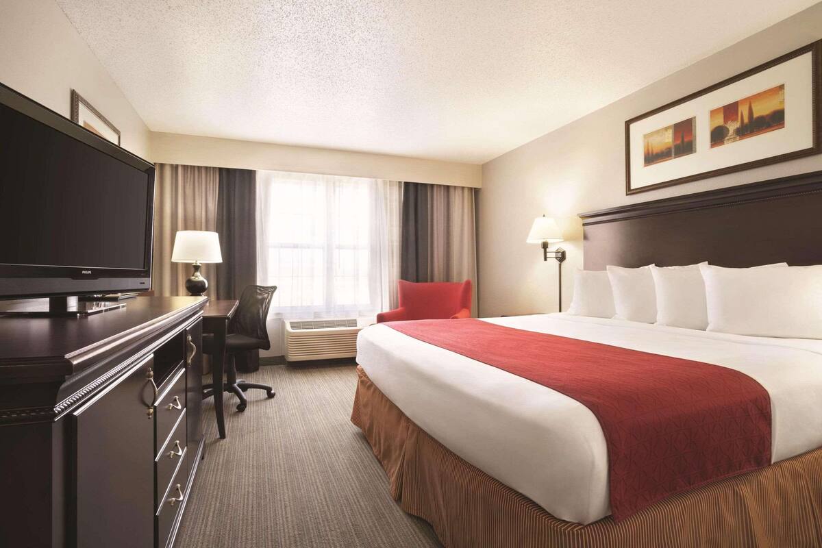 A hotel room with a large bed, a desk with a chair, a television, and a window with curtains.